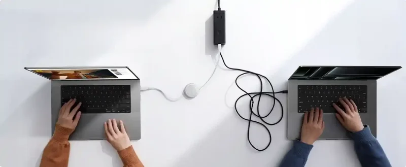 Zwijany biały kabel Baseus 2x USB-C 60W 1m podczas ładowania laptopa na biurku