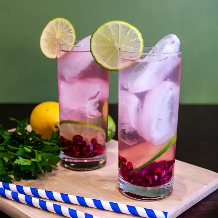 Dwa różowe napoje z dużymi kostkami lodu i plasterkami limonki